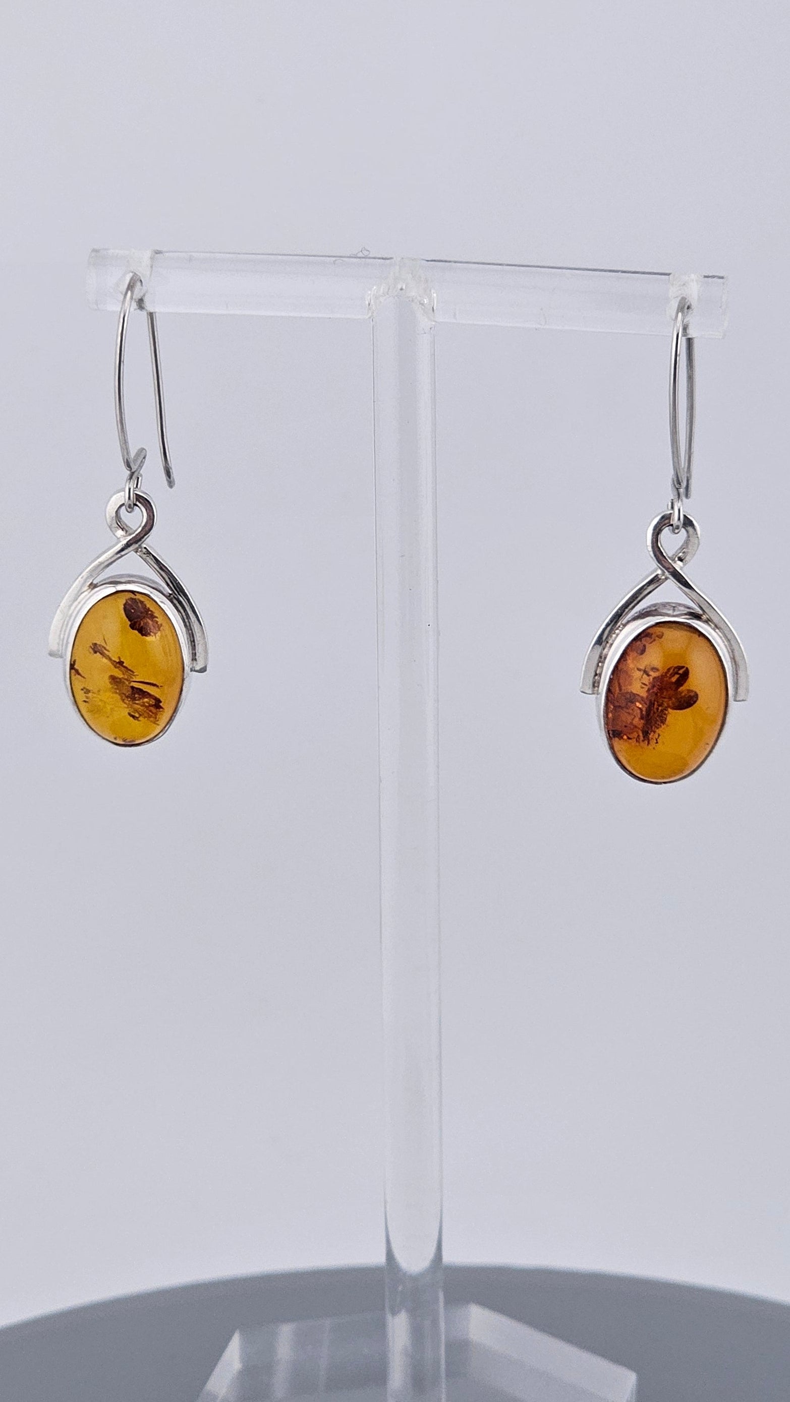 Pair of amber earrings on a clear stand against a white background