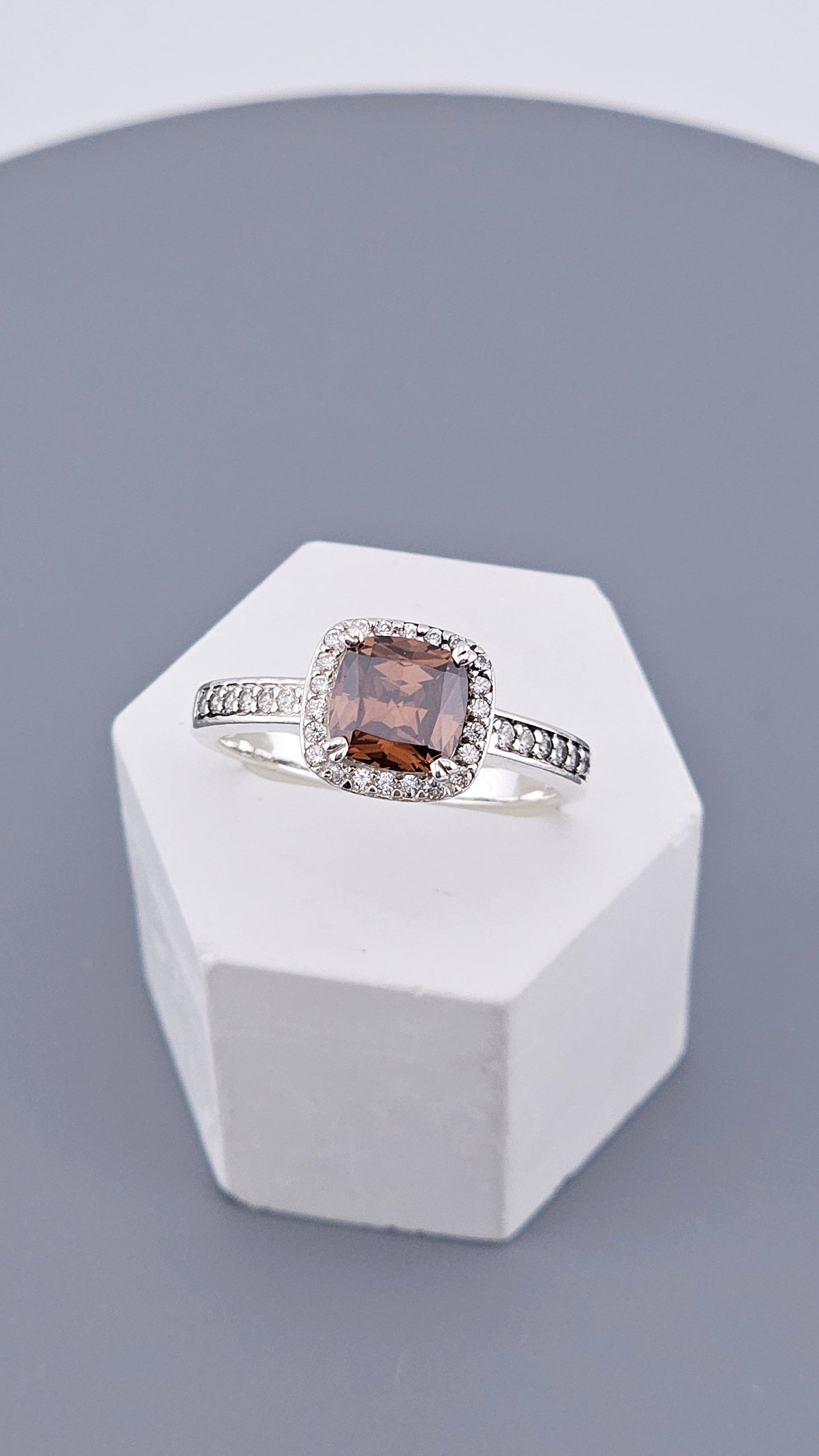 Silver ring with a brown gemstone on a white stand against a gray background