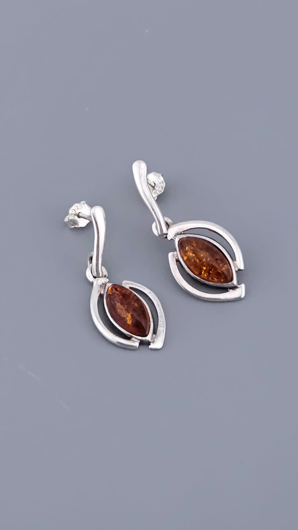 Pair of silver earrings with amber stones on a gray background