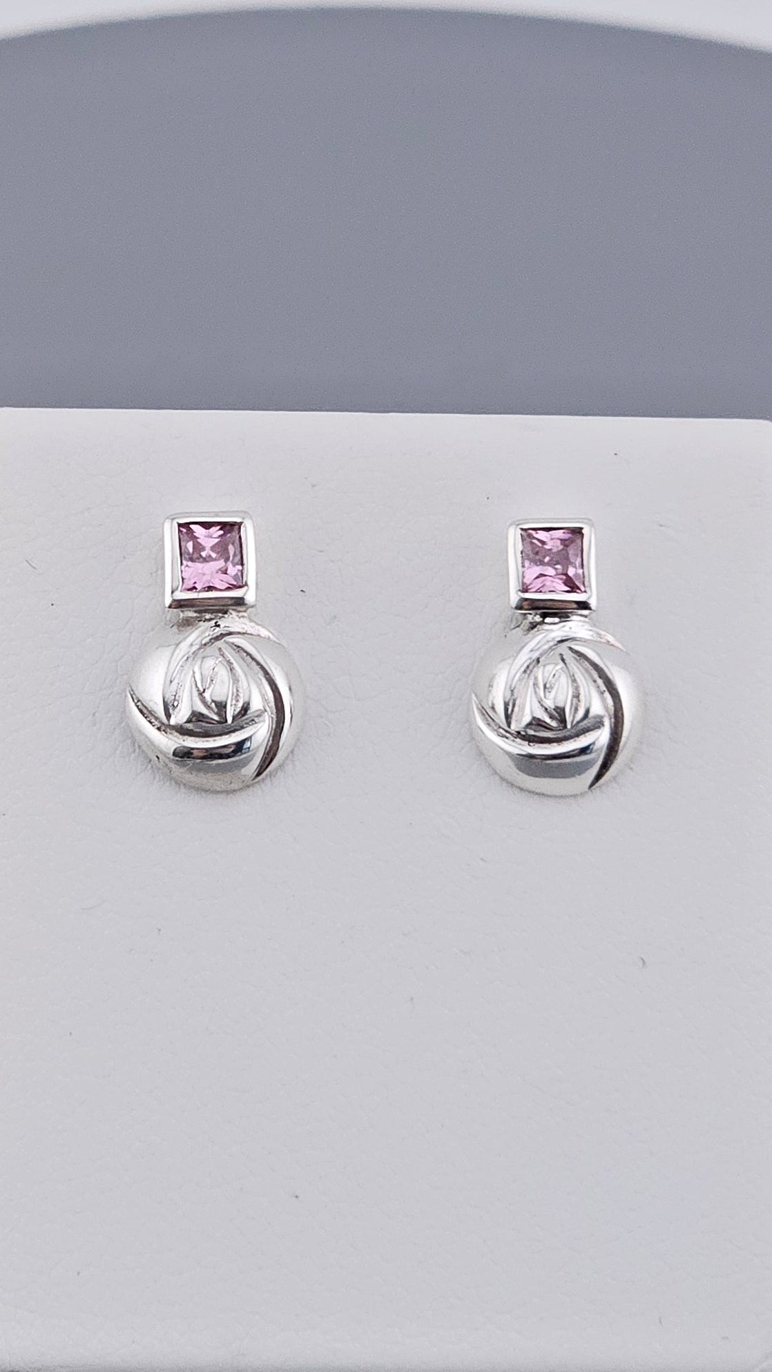 Pair of silver earrings with pink gemstones on a white card against a gray background
