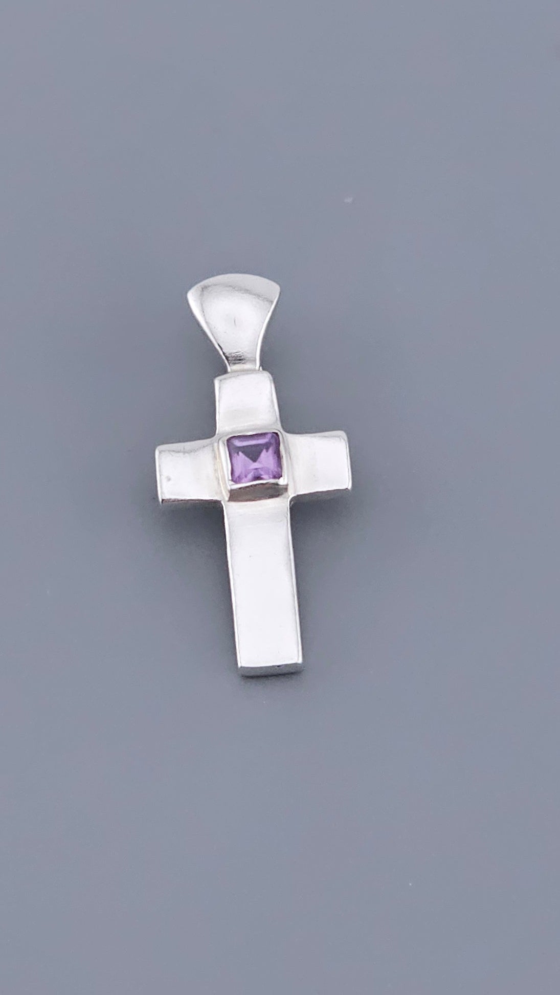 Silver cross pendant with a purple gemstone on a gray background