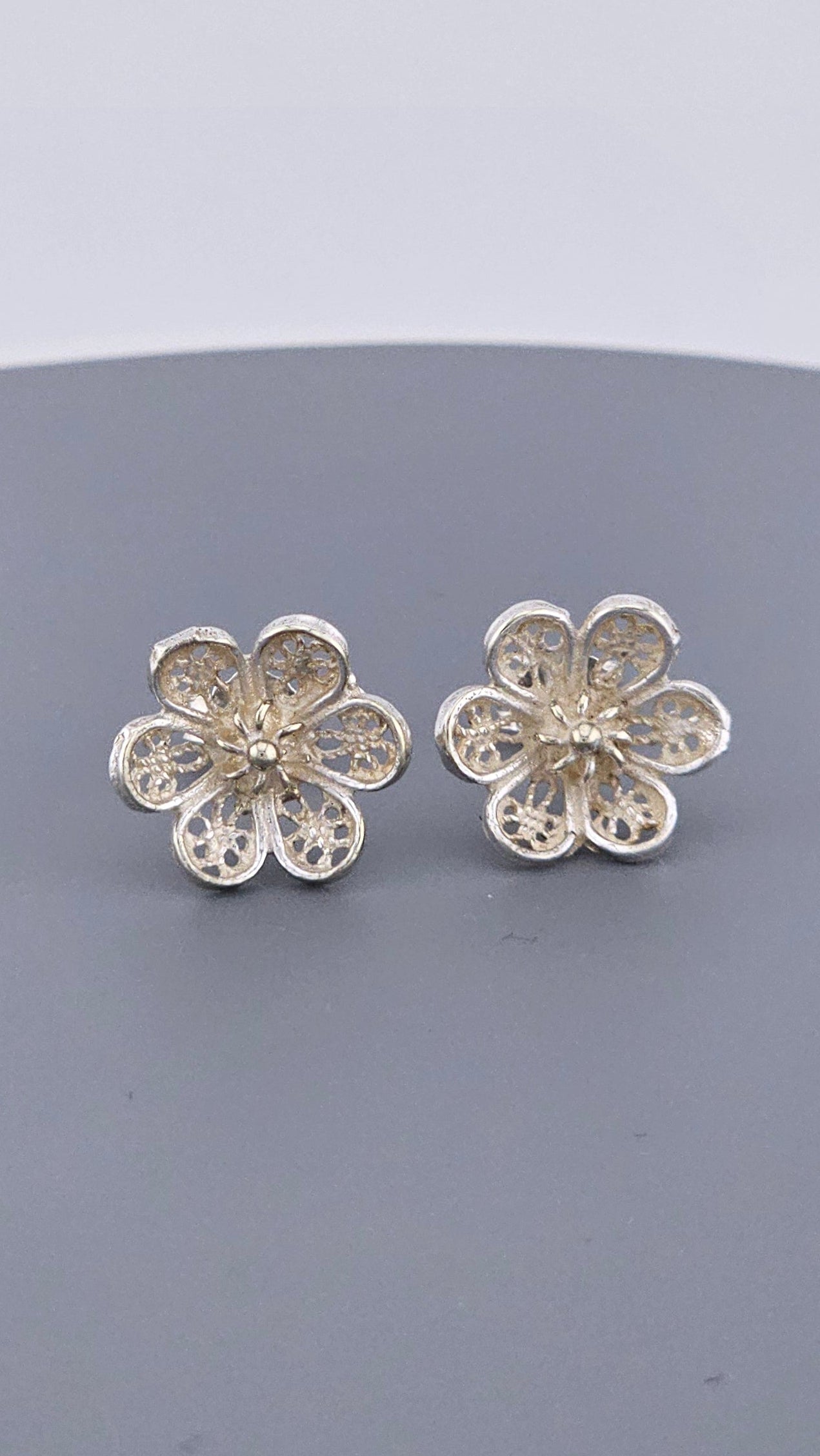 Pair of silver flower-shaped earrings on a gray background