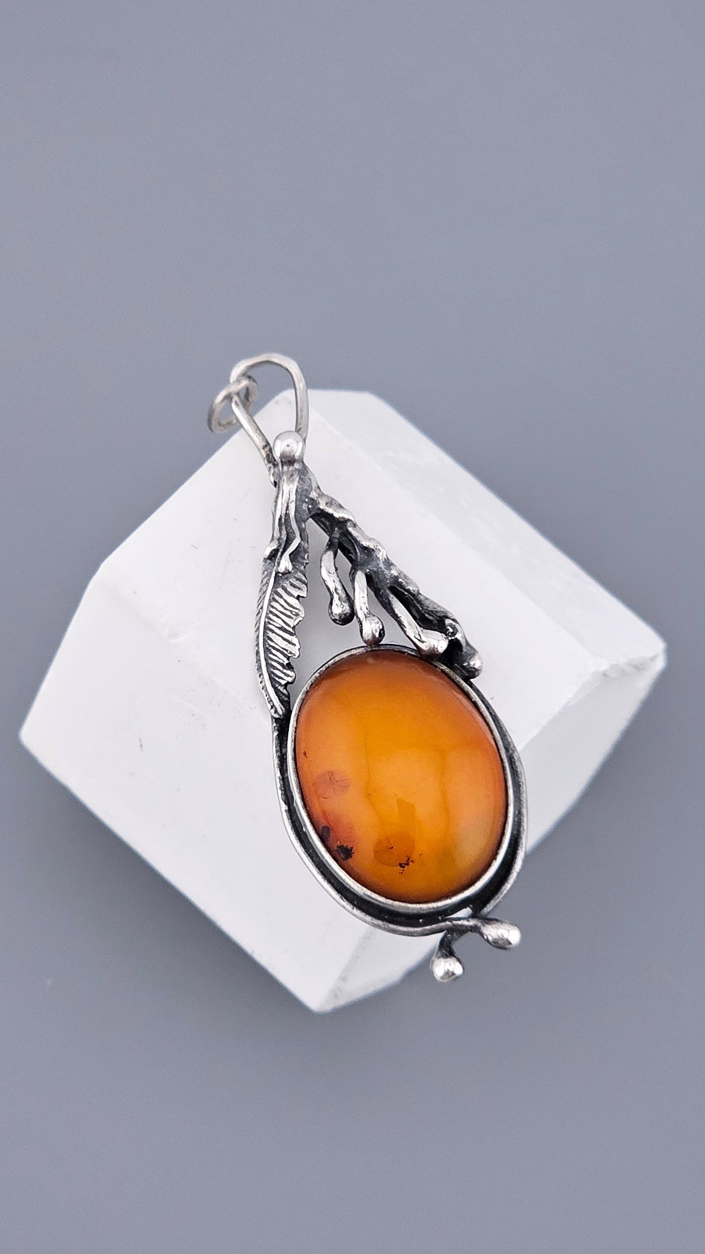 Silver pendant with a amber stone on a white cube against a gray background