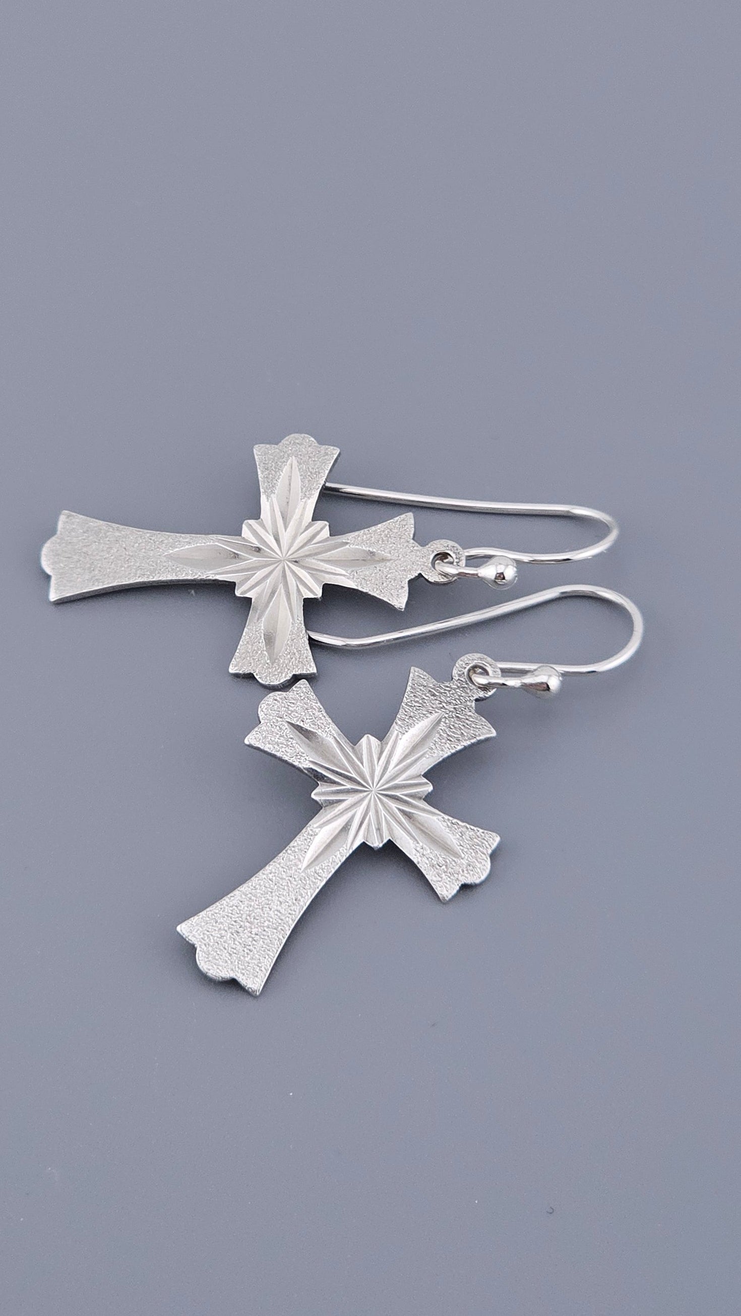 Silver cross-shaped earrings on a gray background